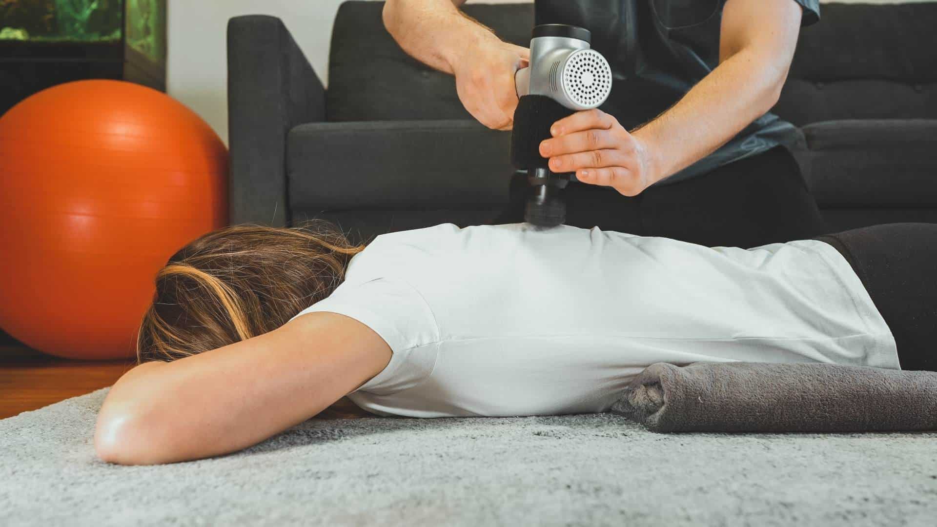 massage therapist using a percussion massage gun on back